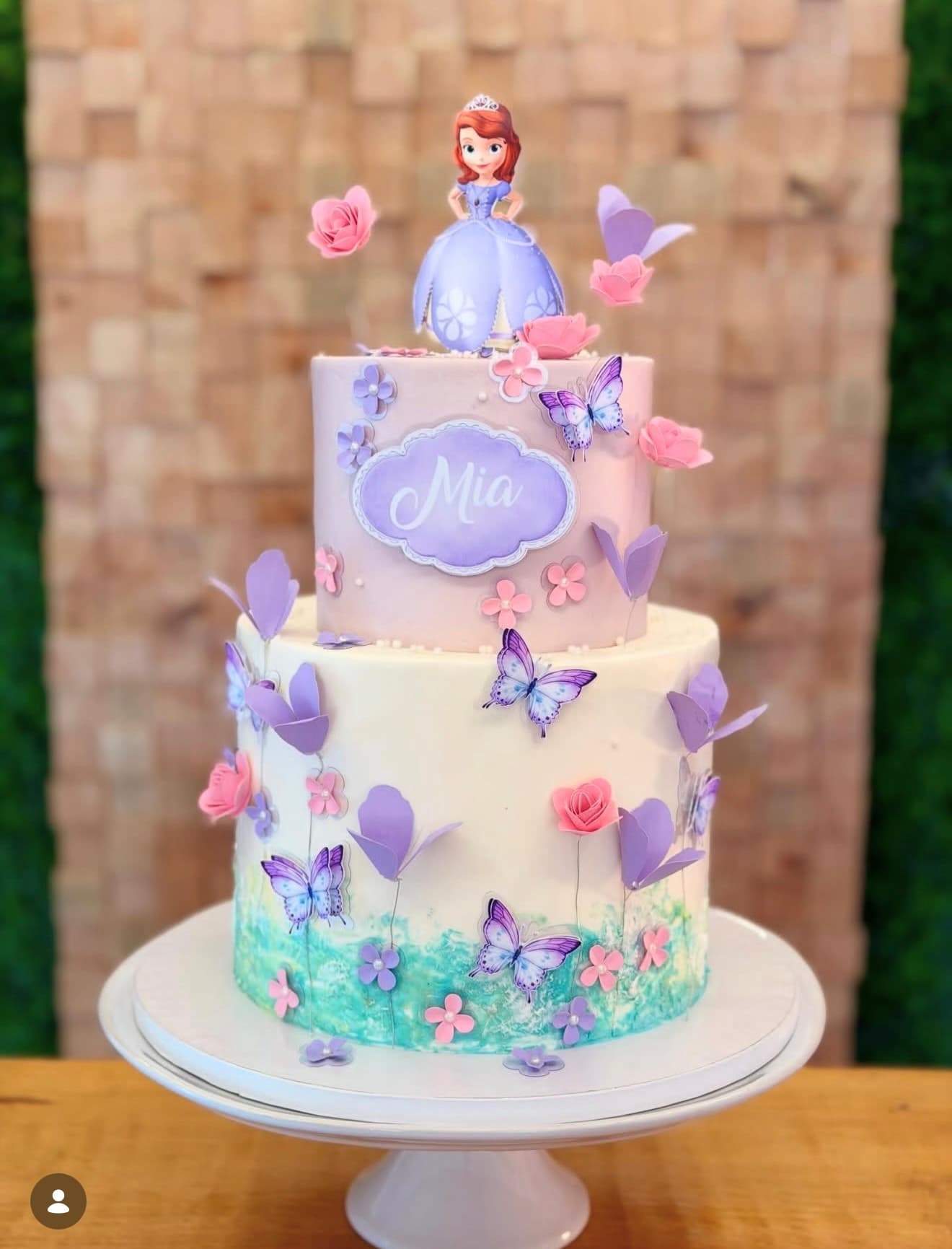 Princesa Sofia — Bolo em tons lilás e rosa com borboletas, flores e jardim pintado à mão na base.