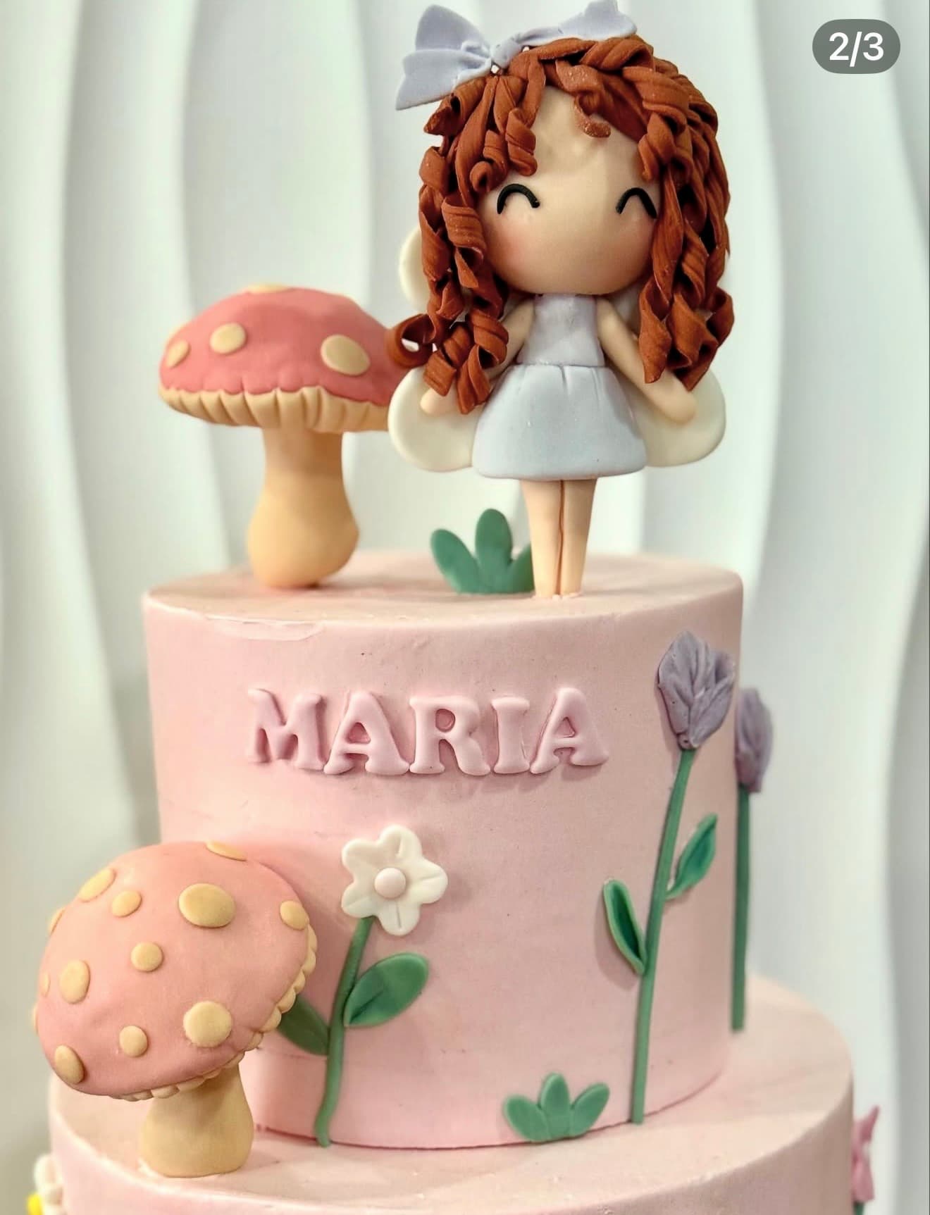Boneca Encantada — Bolo rosa delicado com boneca de caracóis modelada, cogumelos e flores em pasta de açúcar.